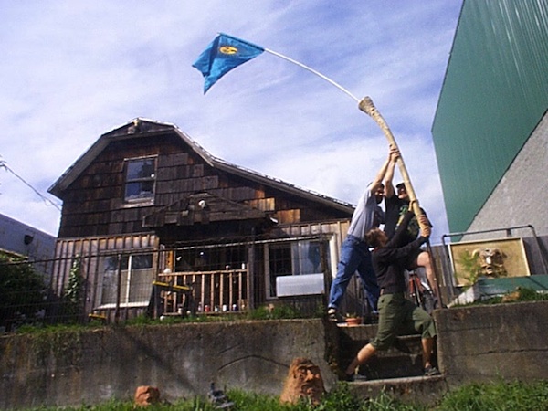 Photo of flagraising at Monkeyhut,
                                a beat-up old rental shack in what used
                                to be Fremont, Seattle, circa 2001